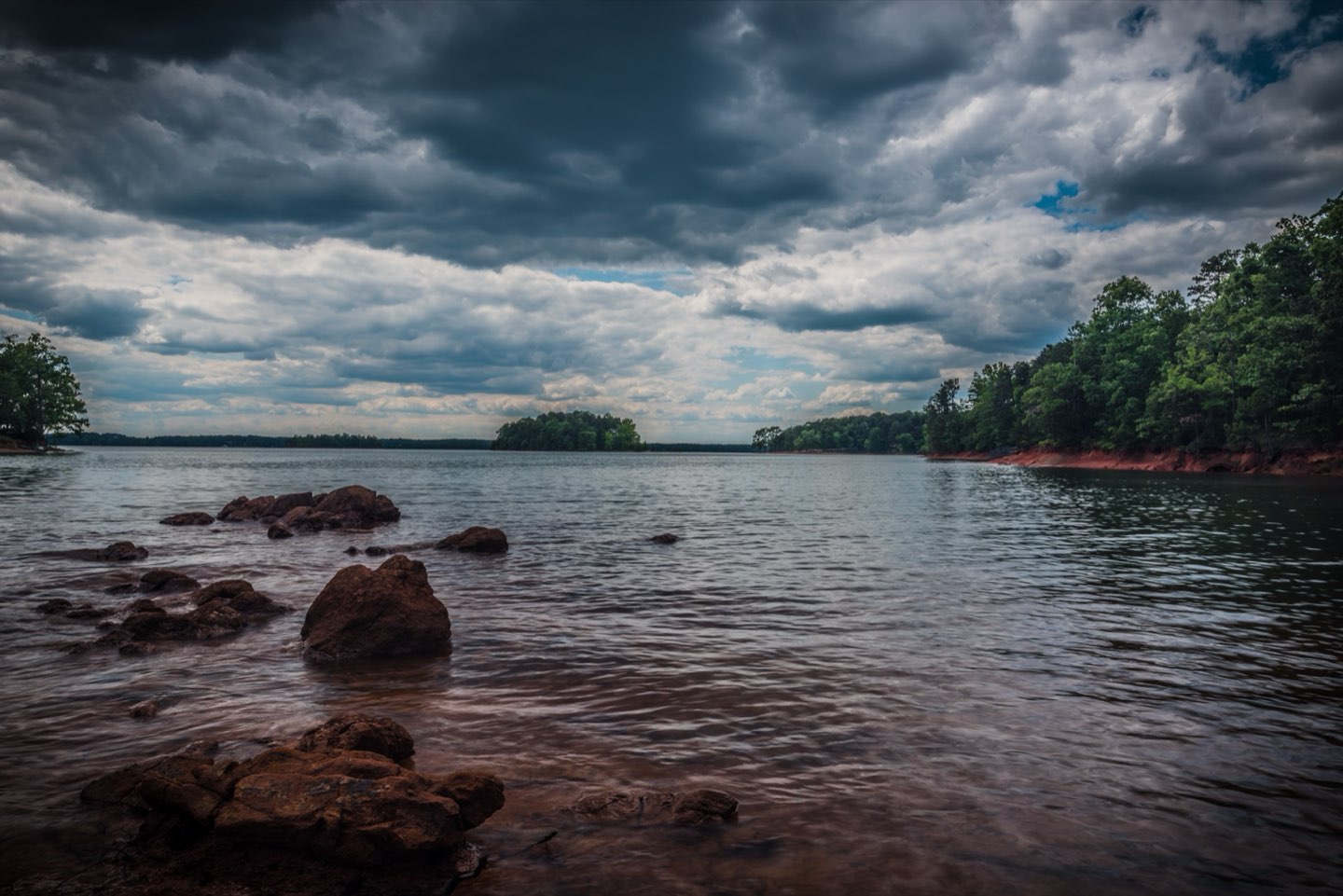 Broken storm sky over open water at Lake Hartwell, red-clay boulders along the shoreline