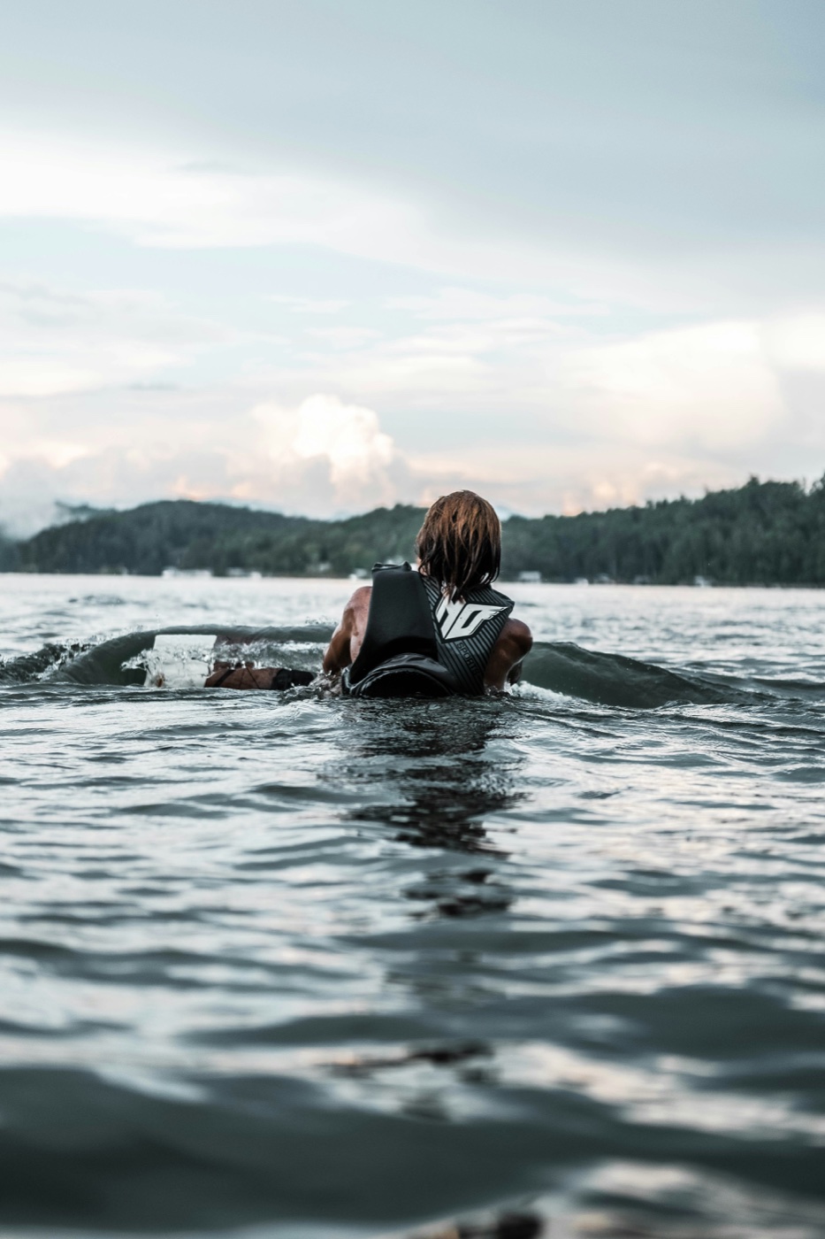 A wakeboarder in the water on Lake Keowee at dusk, forested ridge behind