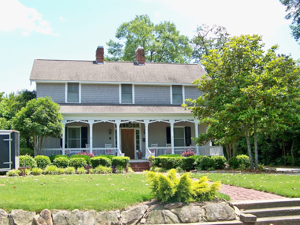 A restored two-storey home in Belton with a white columned porch, rocking chairs and mature landscaping